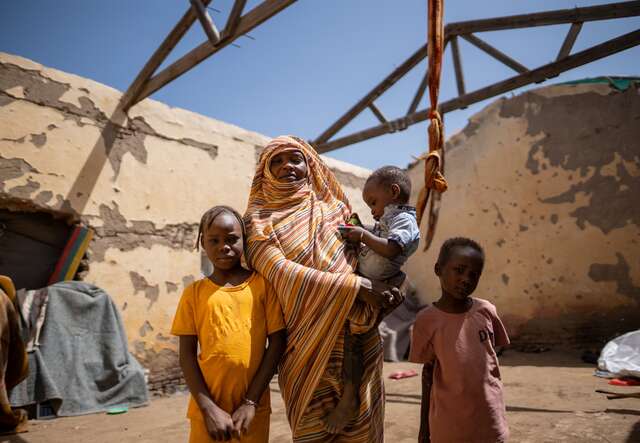 Eine Mutter hält ihr kleines Kind in den Armen. Zwei andere Kinder stehen neben ihr in einer Notunterkunft in Sudan..