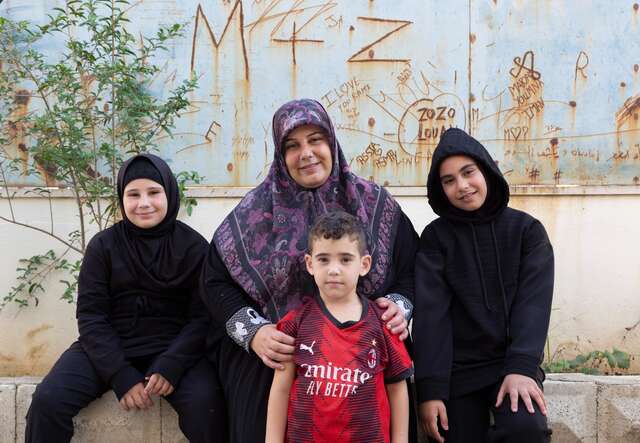Eine Mutter sitzt mit ihren drei Kindern im Freien. Die Familie ist aus ihrer Heimat im Libanon vertrieben worden.