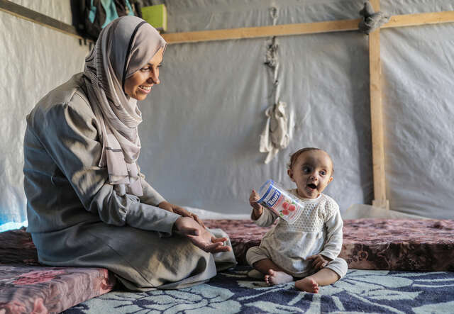 Mamman Alaa sitter på golvet i ett tält och leker med sin sju månaders gamla dotter. De bor nu i flyktinglägret Shams i Gaza.